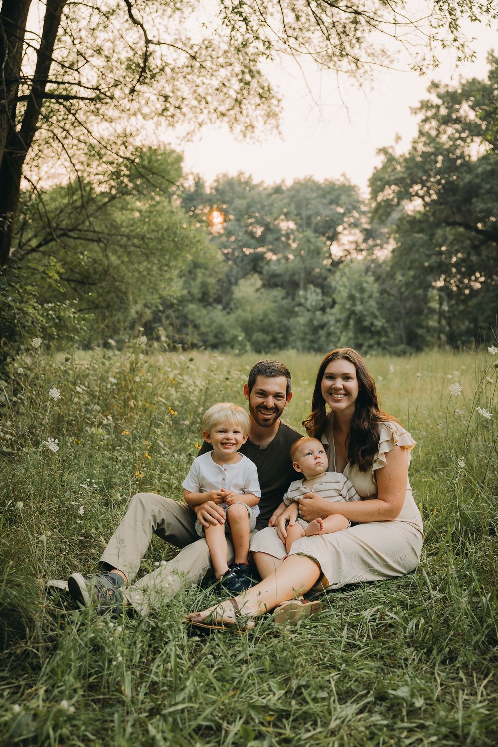 A family relaxes together in a sunlit meadow filled with wildflowers during a summer evening.