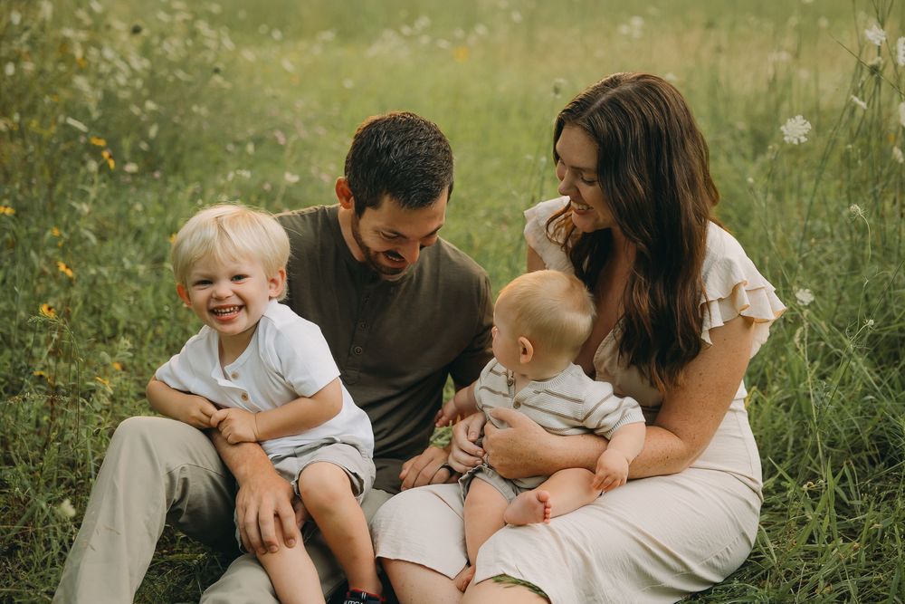 A family sits together on grass in a field during a golden hour photoshoot.