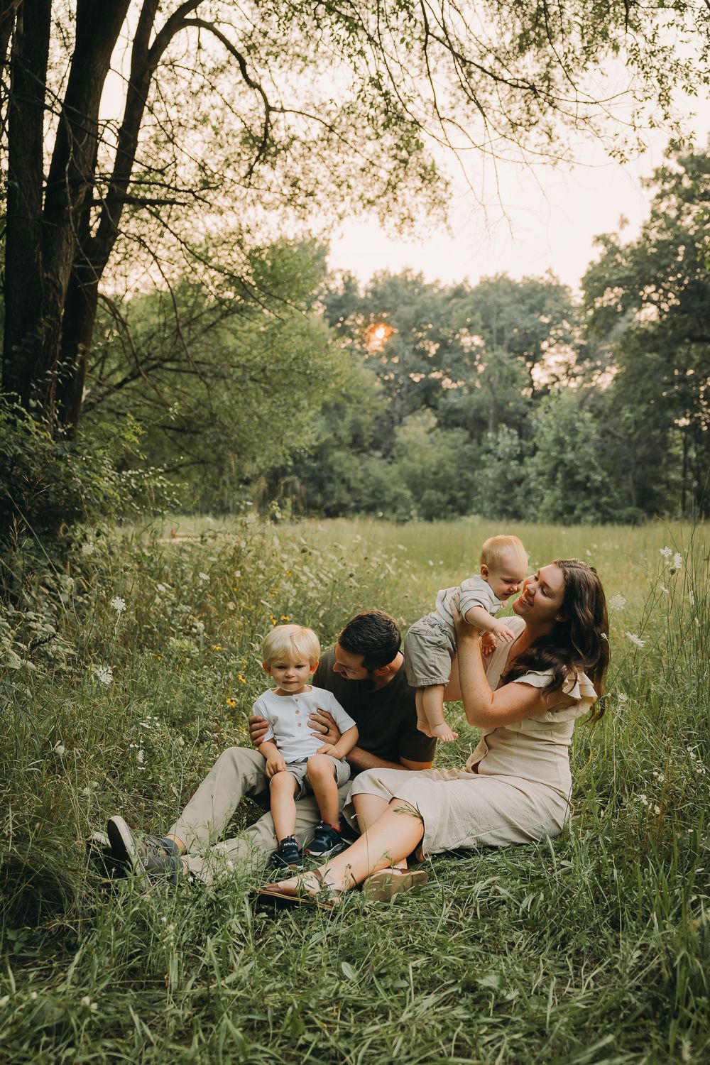 A joyful outdoor portrait of a family spending quality time together in a lush green field at sunset.