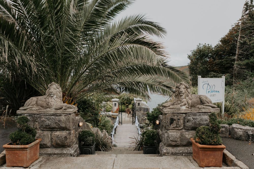 Stone lion statues guarding the entrance pathway of Polhawn Fort wedding venue with palm trees.