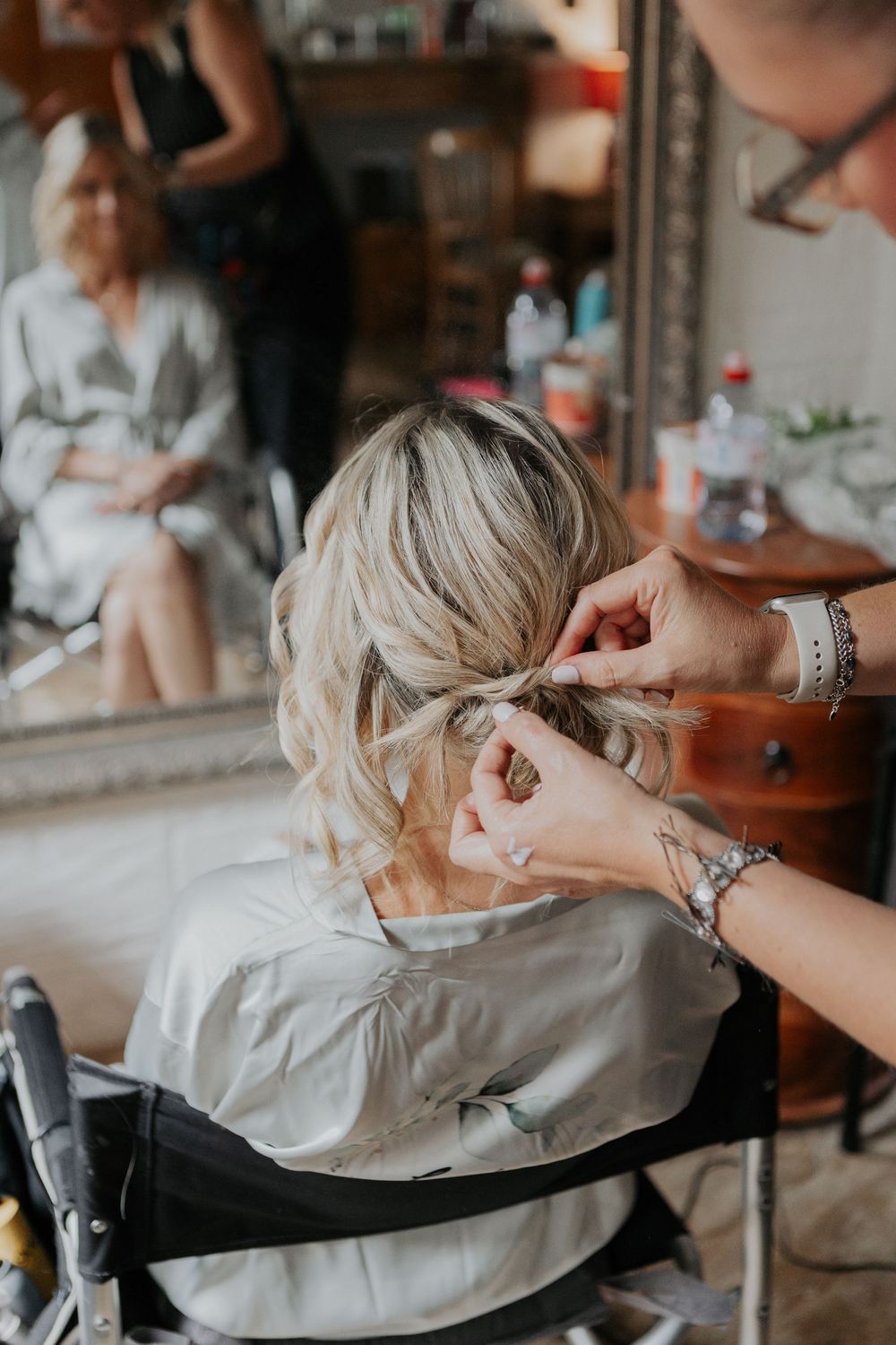 Hairstylist pinning up blonde bride hair in elegant updo before wedding ceremony.