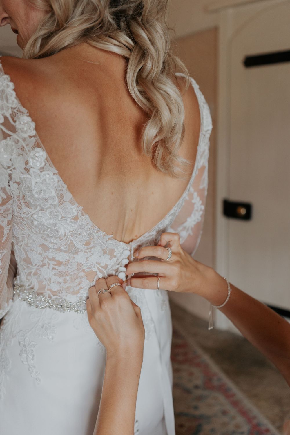 Close-up of hands fastening delicate buttons on the back of a bride's lace wedding dress.