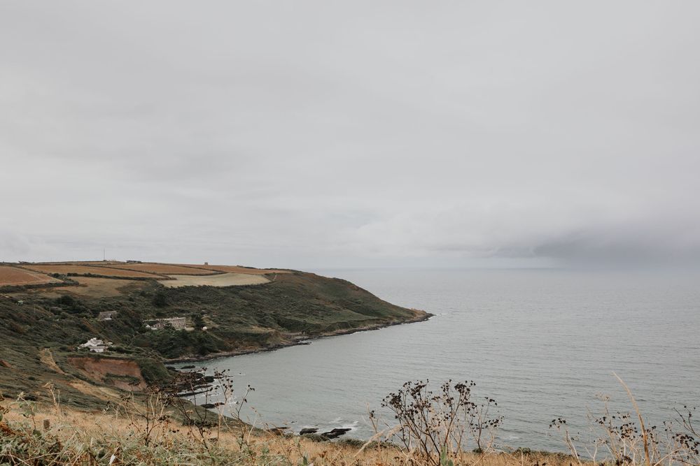 Overcast coastal landscape with rolling hills and calm grey sea under cloudy sky.