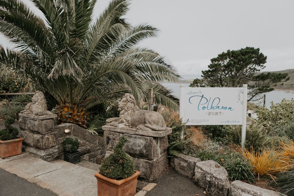 Entrance to Polhawn Fort venue with palm trees and stone lion statues flanking the driveway.