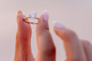 Close-up of hands showing a sparkling engagement ring on a sandy beach at sunset.