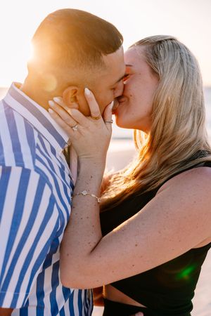 A romantic couple embraces and kisses on the beach during golden hour.