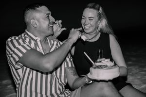A couple shares joyful laughter and kisses on a dark beach at night.