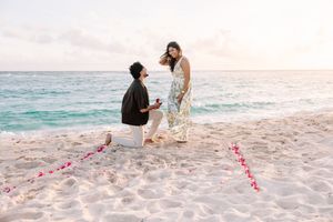 A beach proposal setup with pink flower petals arranged in the sand.