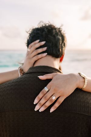 Close-up of hands with engagement ring resting on shoulder at sunset.