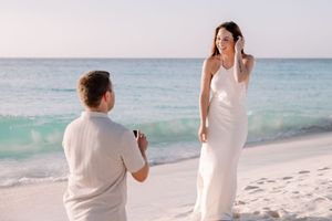 Two people in white clothing walking along a scenic beach with crystal blue waters.