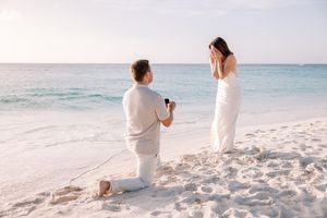 A romantic beach scene with two people in white outfits sitting on pristine sand near turquoise waters.