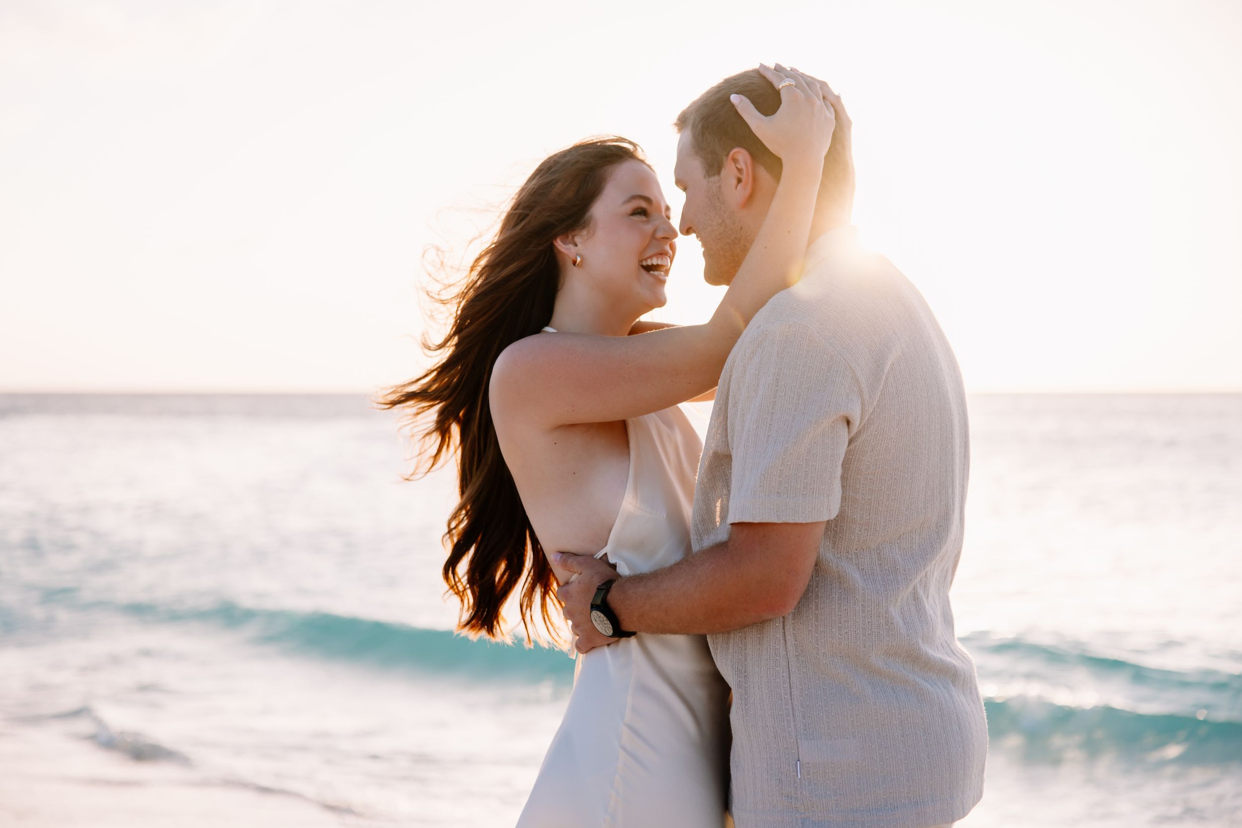 Romantic beachside moment with couple in white clothing during golden hour.
