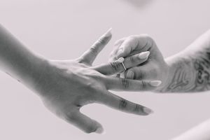 Black and white close-up of hands with wedding rings in artistic composition.