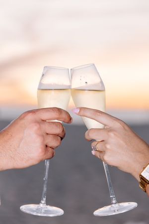 Wine glasses clink together in a celebratory toast against a sunset backdrop.