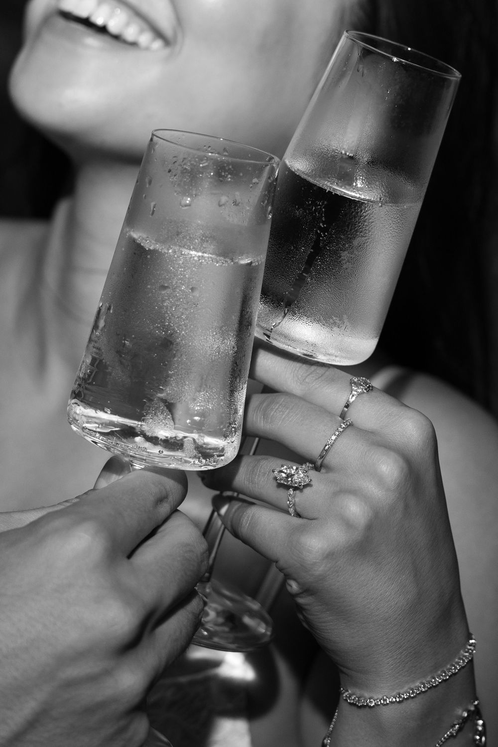 Black and white photo of couple toasting with champagne flutes, woman wearing diamond ring and bracelet.