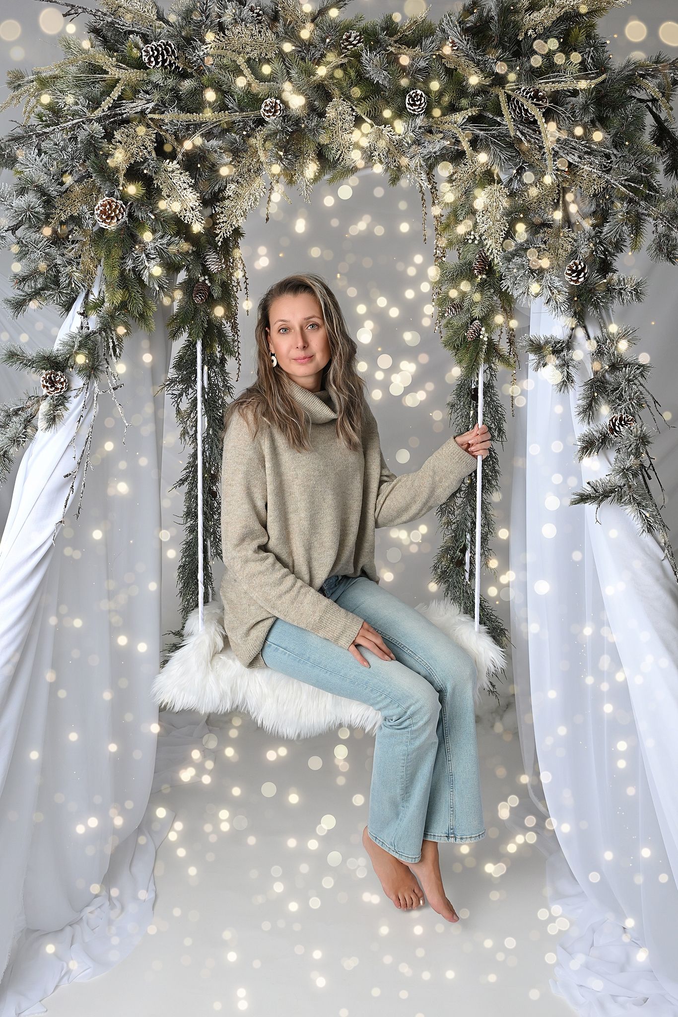 Magical holiday scene with illuminated evergreen arch and twinkling lights on white backdrop.