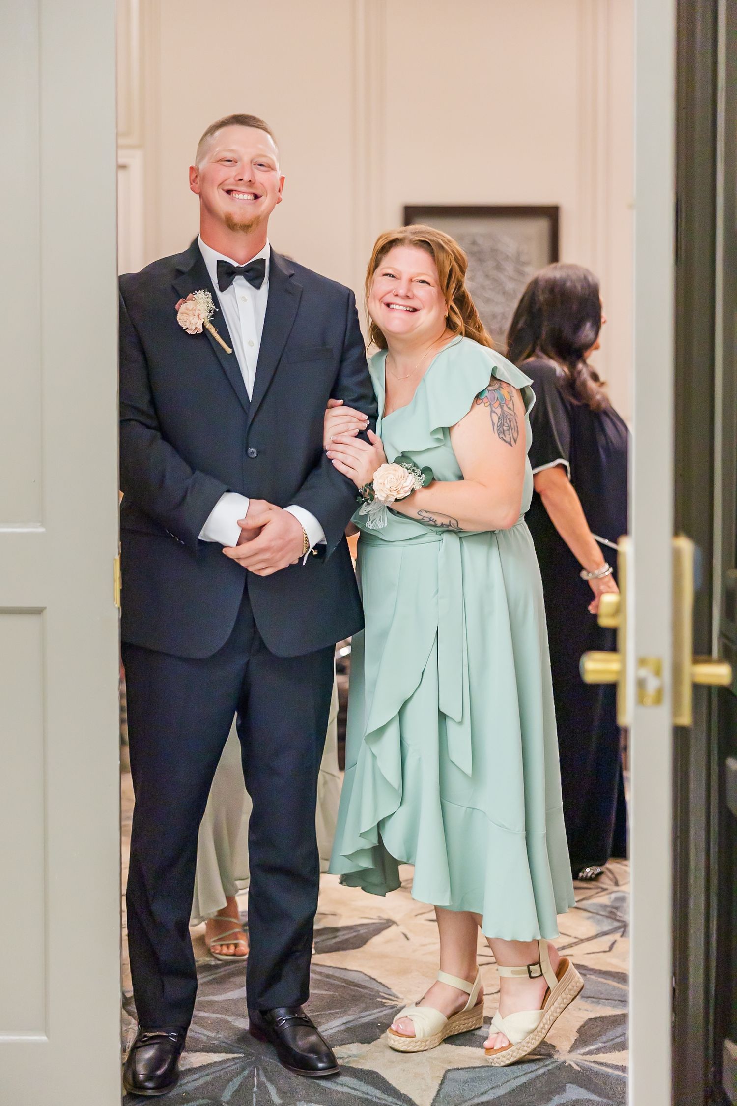 A couple in formal attire shares a joyful embrace at what appears to be a wedding venue in mint green and navy colors.