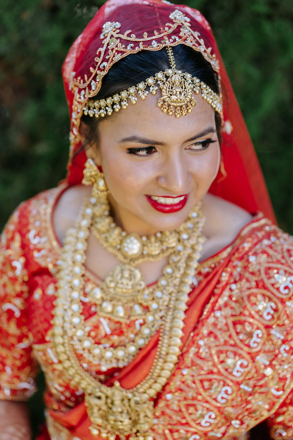 Traditional Indian bride wearing ornate gold jewelry and red bridal attire with detailed embellishments.