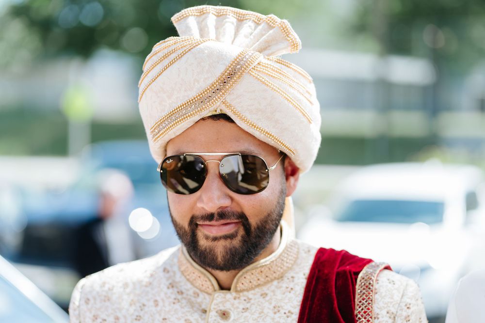 A person wearing a traditional Indian wedding turban and sunglasses smiles during an outdoor celebration.