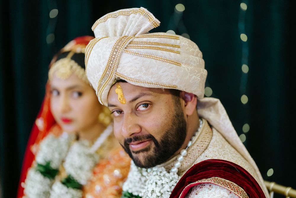 Traditional Indian wedding ceremony with bride in red sari and groom in cream sherwani exchanging vows.