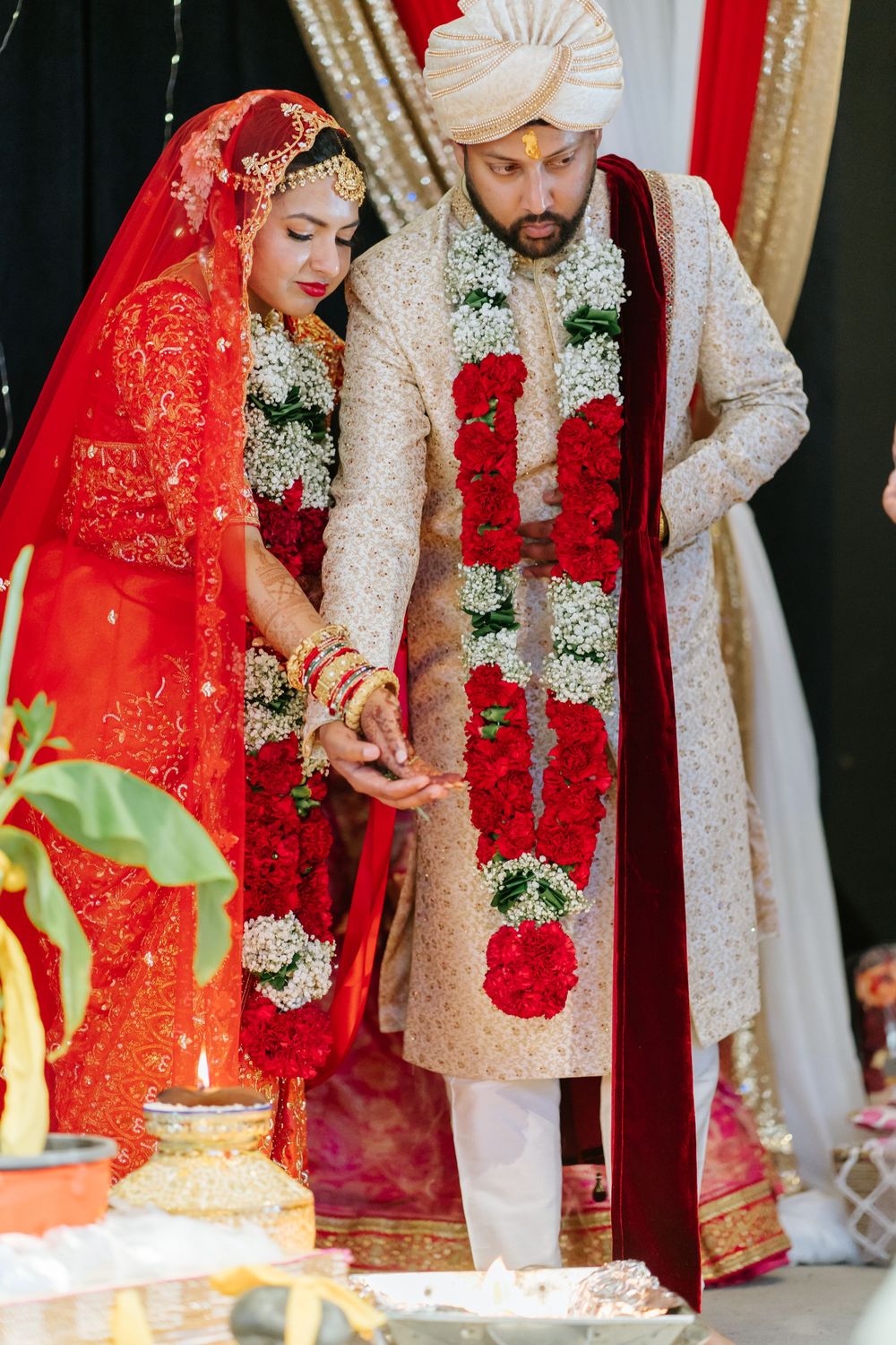 Couple in traditional Indian wedding attire performing ceremonial rituals at decorated mandap.