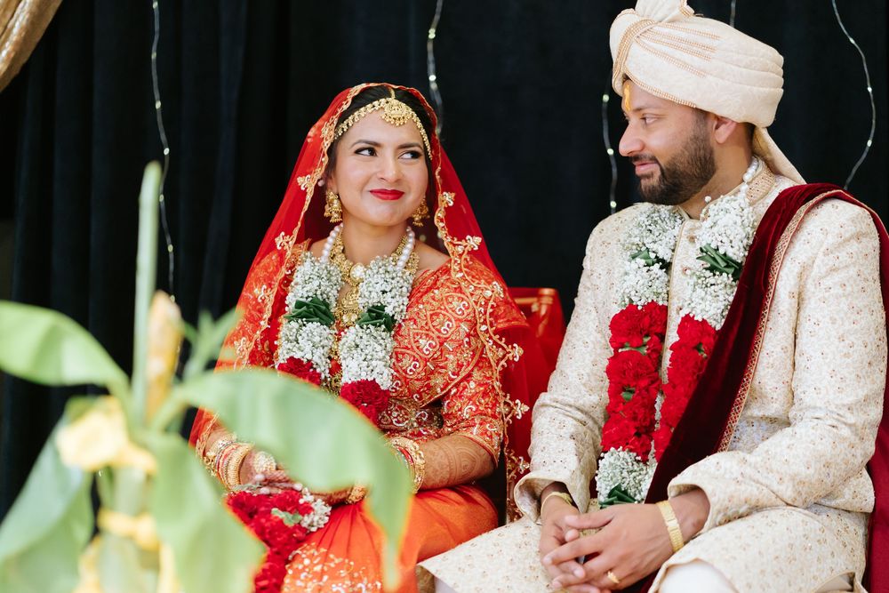 A couple in traditional Indian wedding attire, with the bride in red and groom in white, during their ceremony.