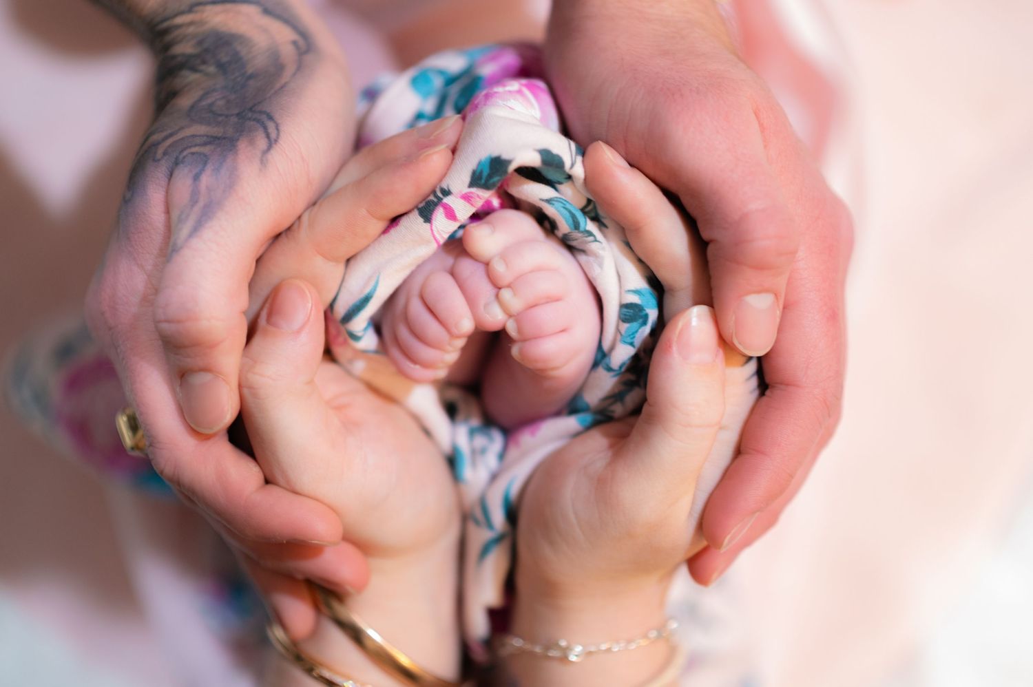 Close-up of hands with colorful rings intertwined against a soft pink background.