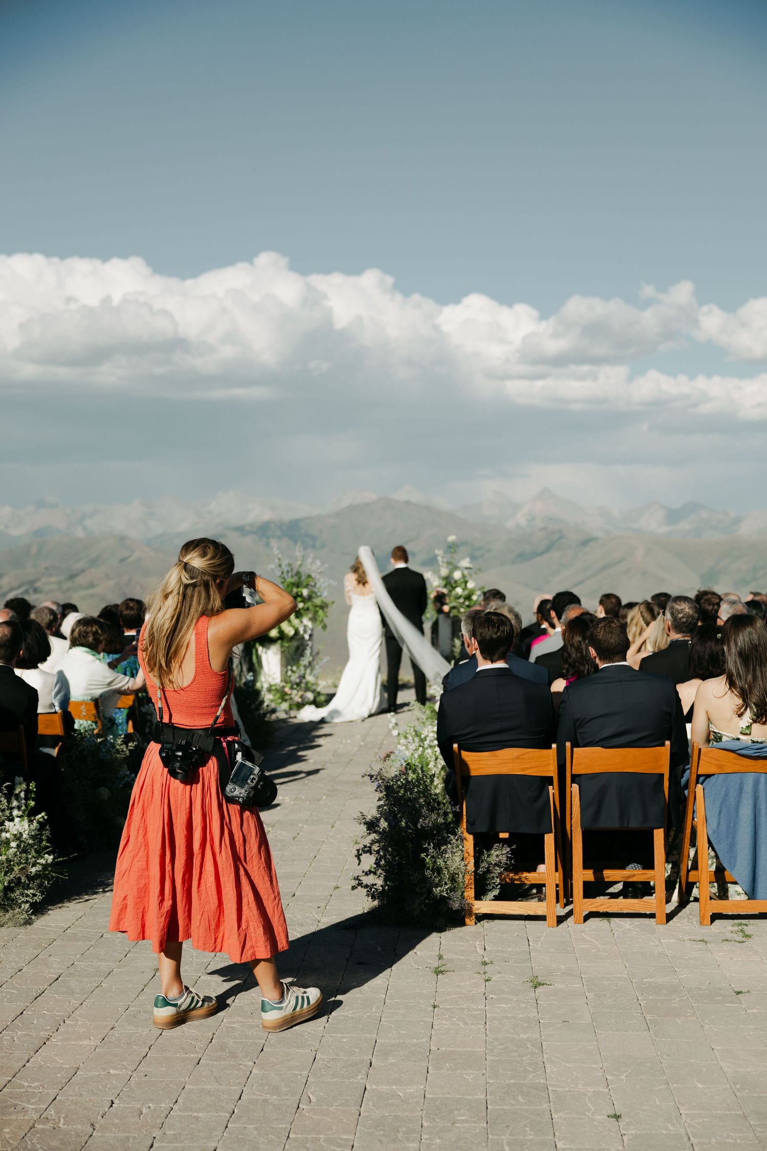 Outdoor wedding ceremony setup with wooden chairs and mountain views under a bright blue sky.