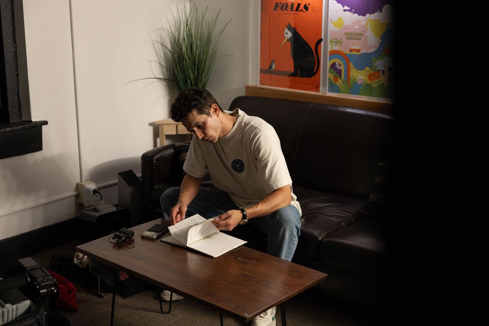Man leaning over a wooden coffee table reviewing documents in a modern living room with dark leather sofa.