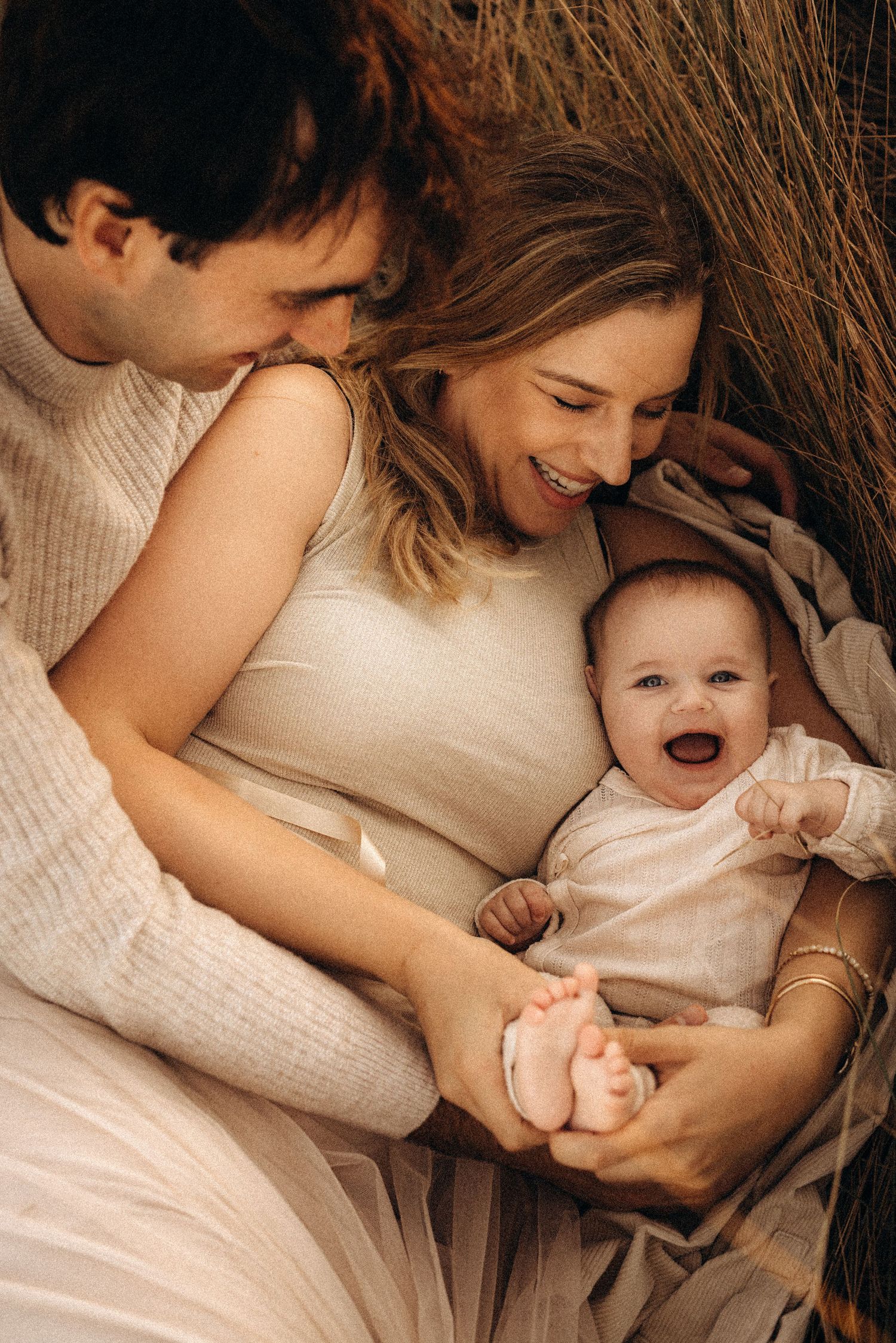 A tender moment between parent and child lying together in soft white clothing against neutral bedding. Javea photographer