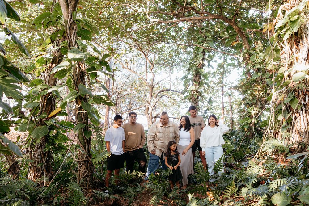 Wedding party poses together in a lush tropical garden setting with natural sunlight filtering through the trees.