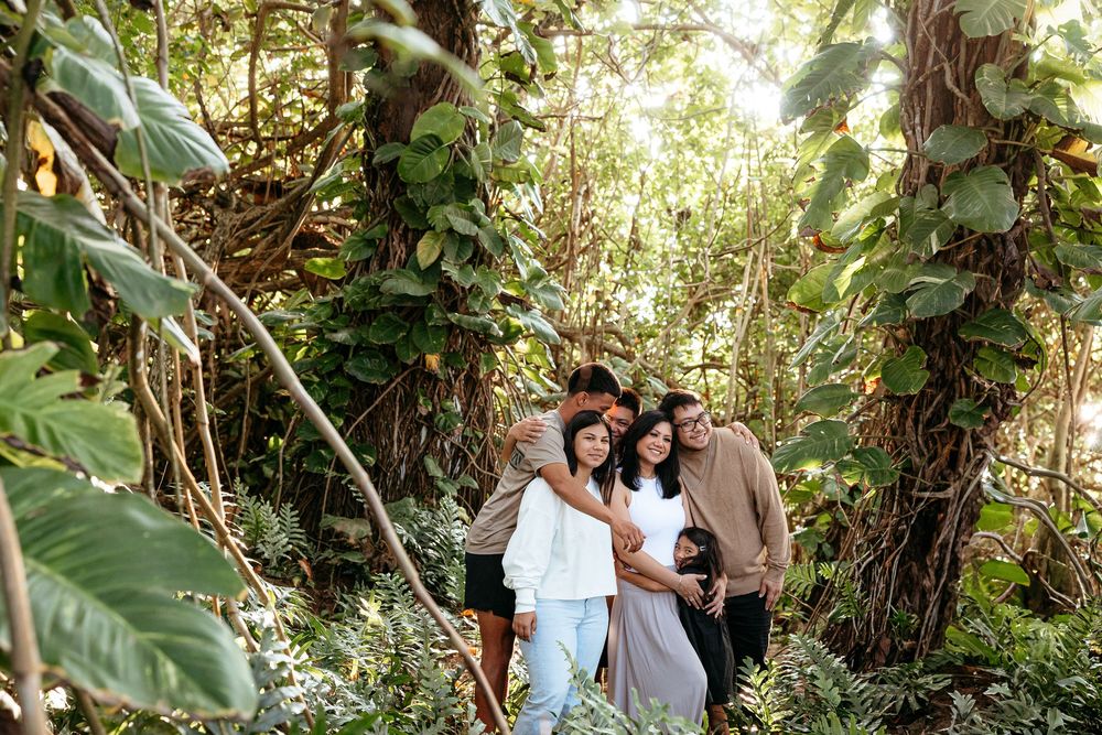 A couple poses together in a lush tropical garden setting with sunlight filtering through the trees.