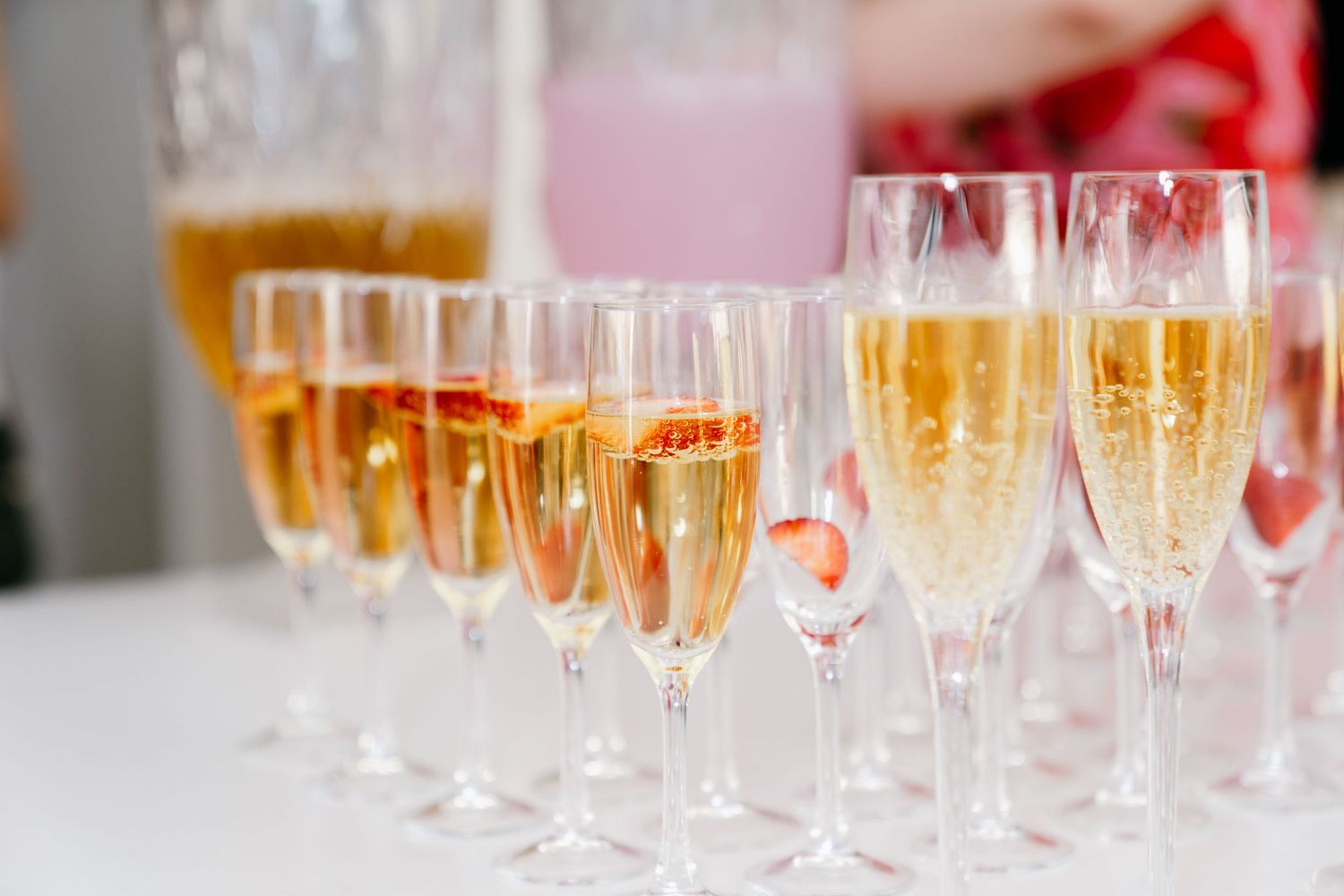 Row of champagne flutes filled with sparkling wine lined up on a white tablecloth.