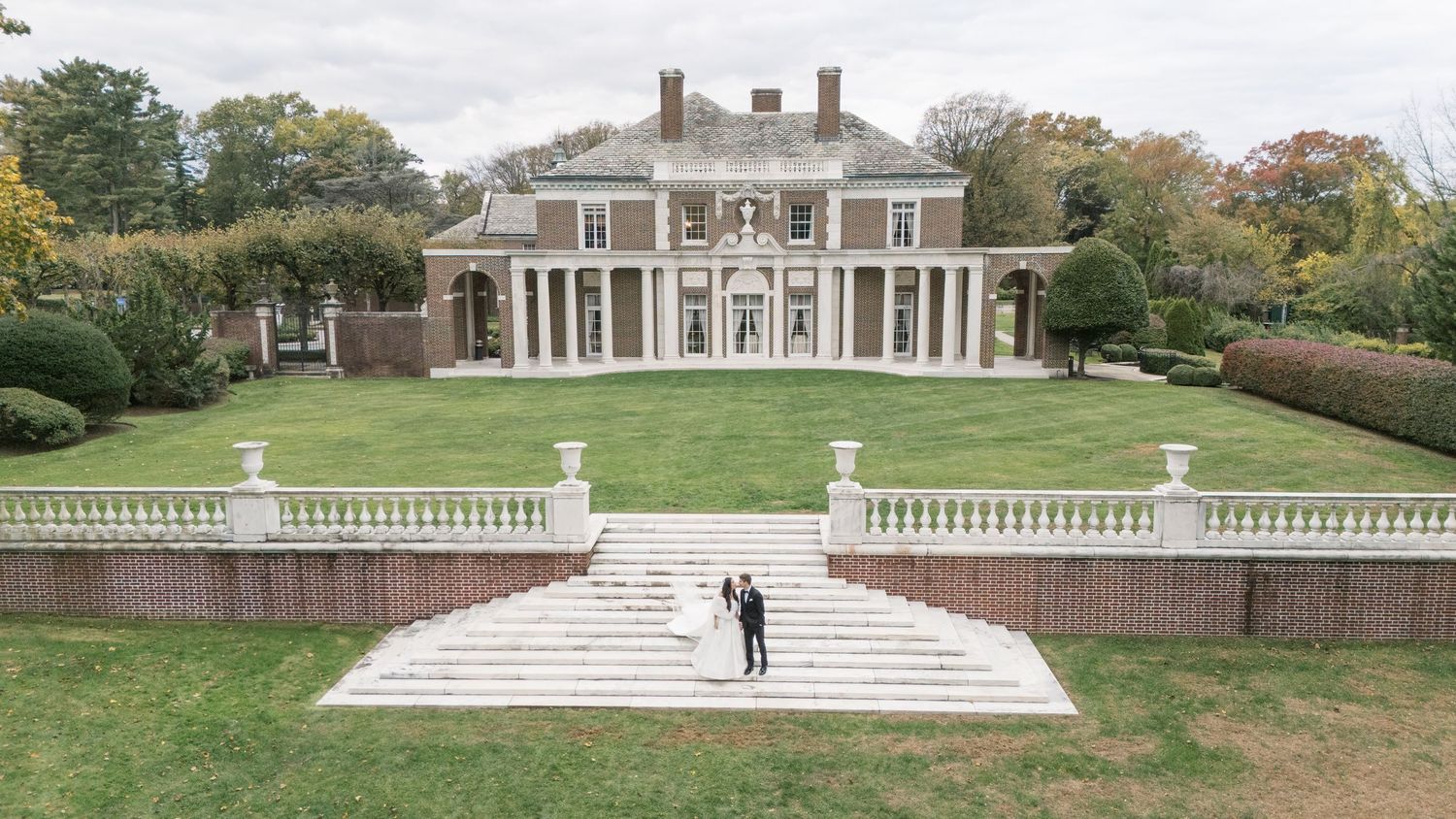 Panoramic view of a stately mansion with classical columns and manicured grounds.