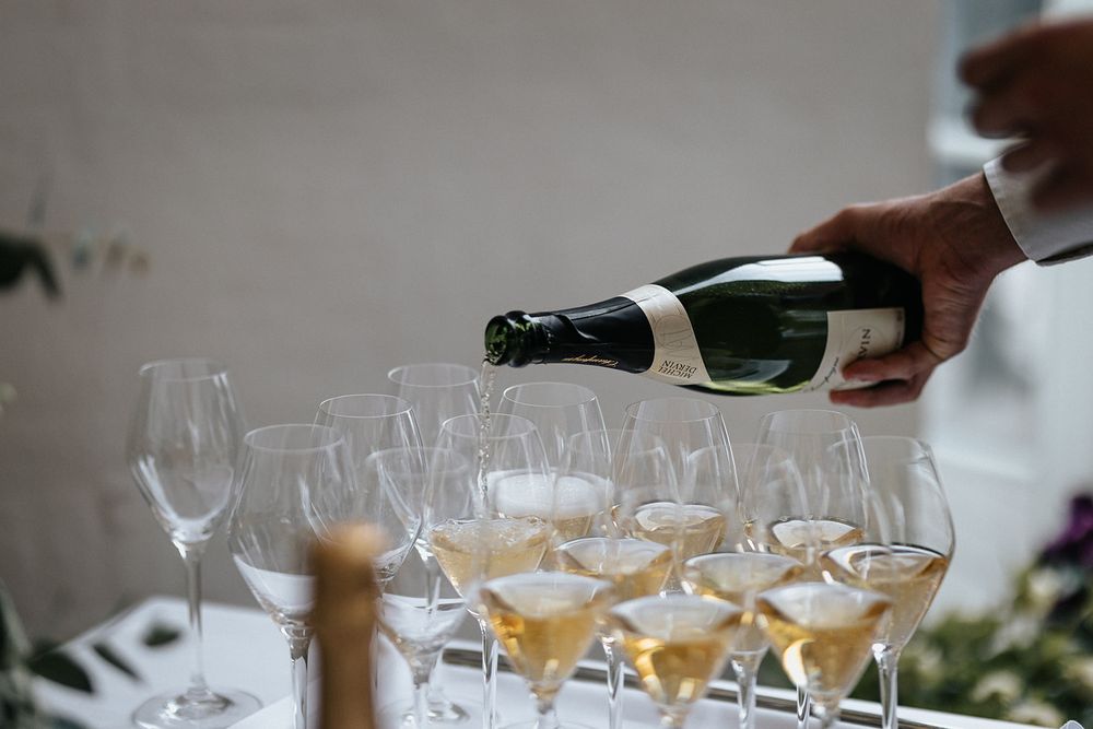 A hand pours champagne into multiple elegant wine glasses arranged on a white surface during a formal event.
