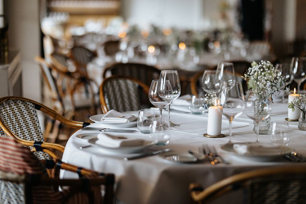Elegant table setting with white linens, wine glasses and baby's breath centerpieces in a rustic restaurant interior.