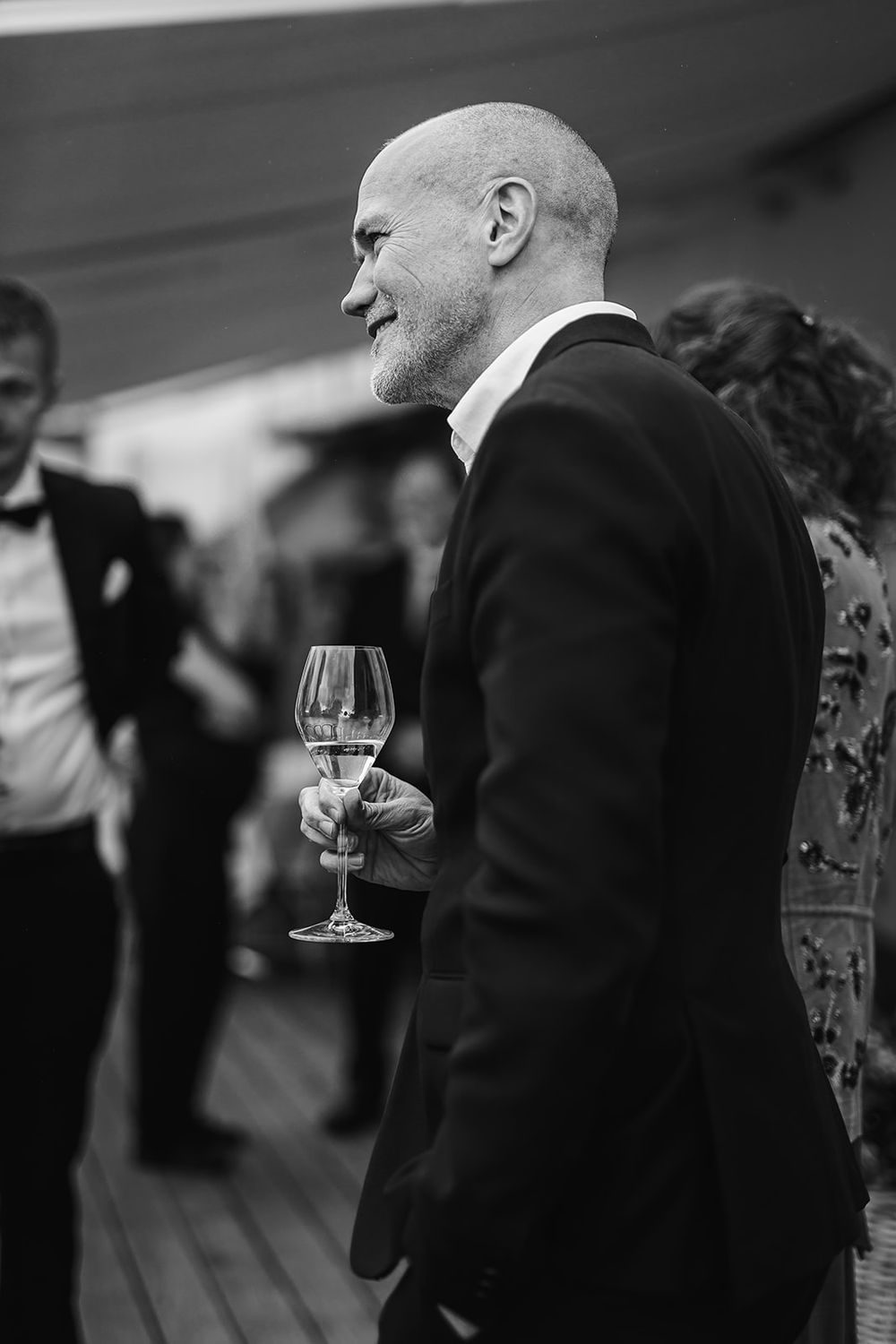 Black and white image of people at an event holding wine glasses in a social gathering atmosphere.