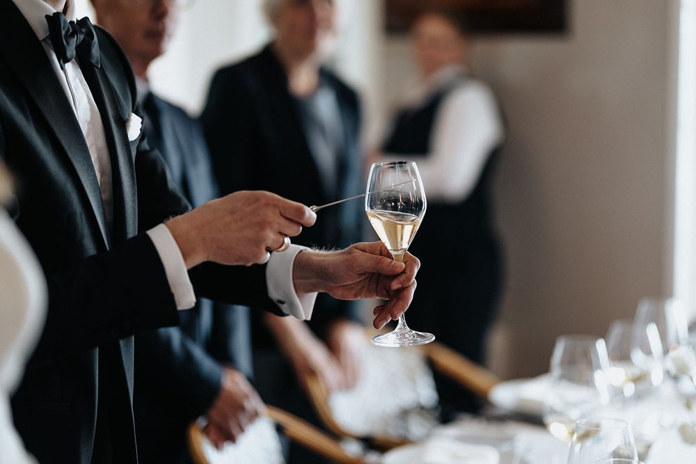 Wedding reception table setting with wine glasses and guests in formal attire.