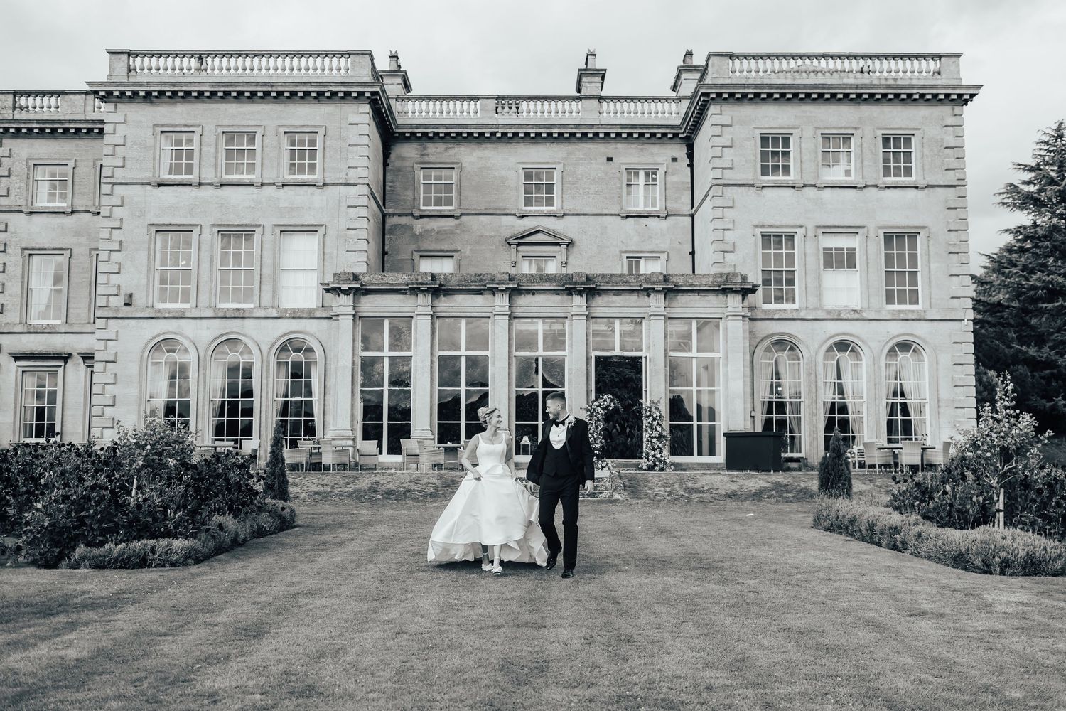 Elegant wedding party poses in front of a grand historic mansion with classic Georgian architecture and manicured gardens.