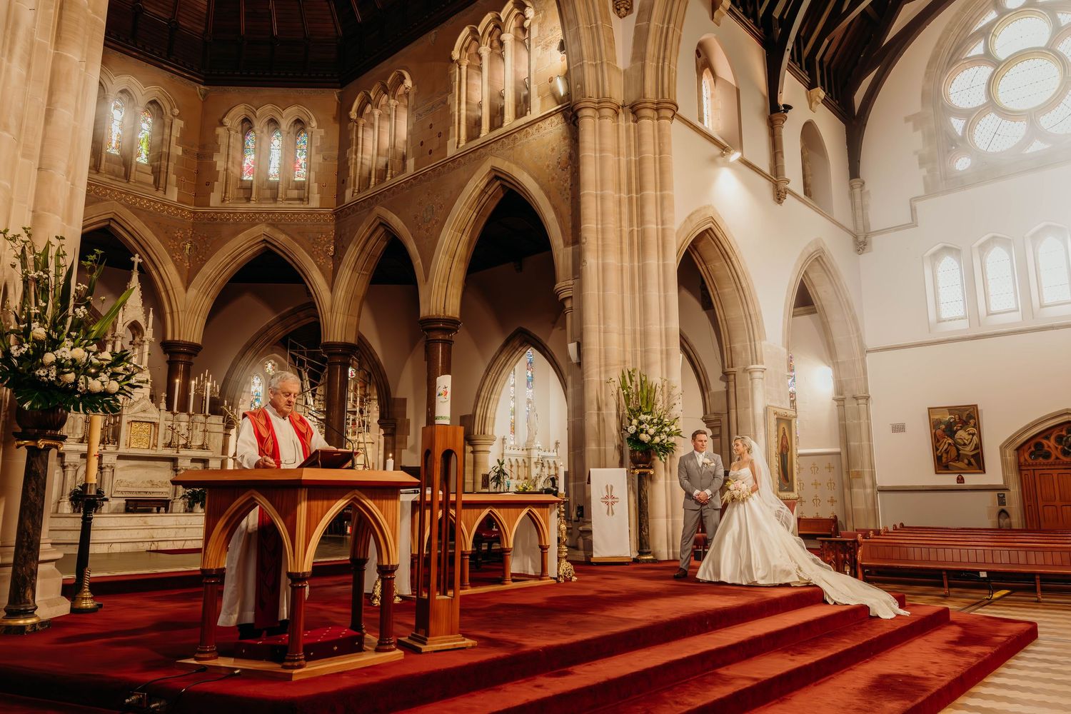 Panoramic view of an ornate church interior with red carpeted aisle and Gothic arches leading to the altar.