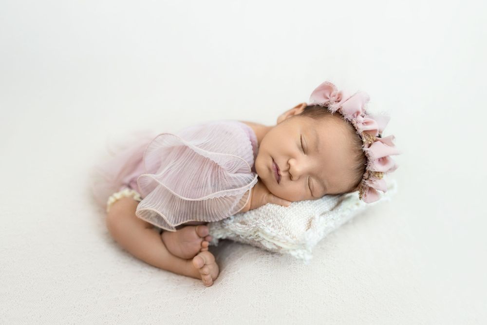 Sleeping newborn baby wearing pink floral headband and delicate lace wrap in artistic studio portraits.