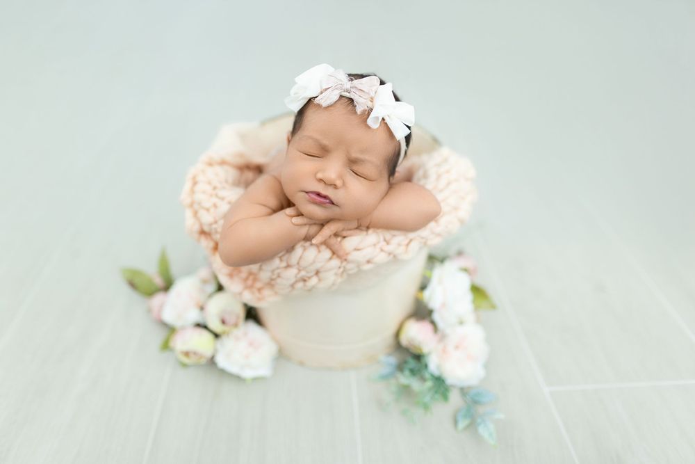 Peaceful newborn baby sleeping on mint green backdrop with soft white flowers and gentle studio lighting.