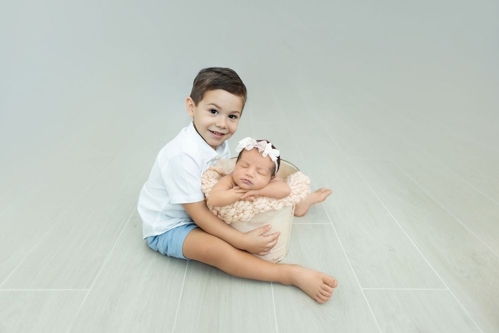 A child lies on a light gray floor in a playful pose wearing casual clothing and smiling.
