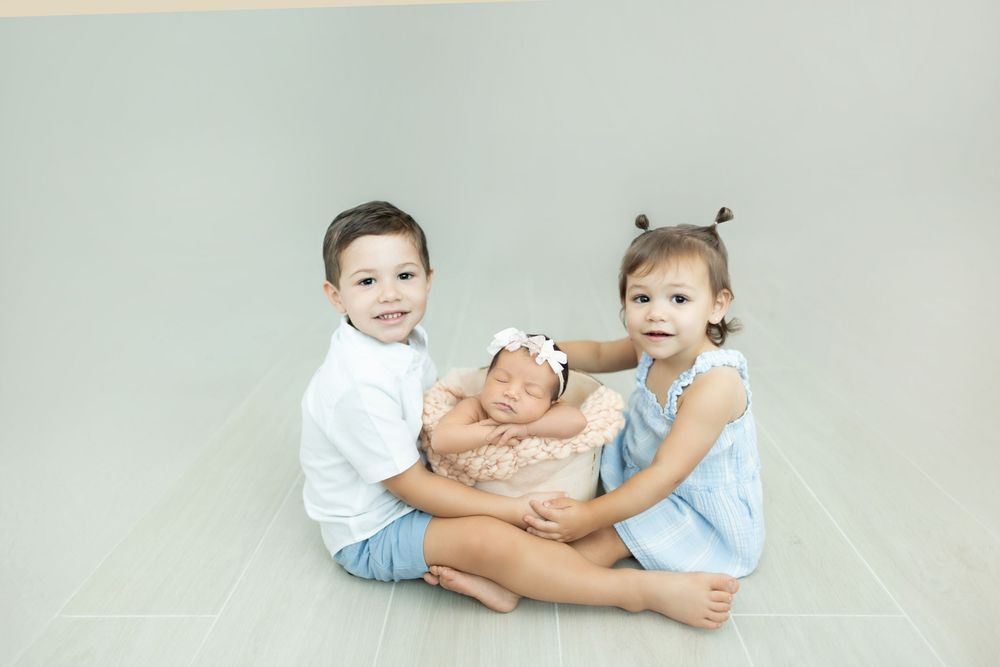 Two young children in light colored outfits playfully interact while sitting together on a light gray background.