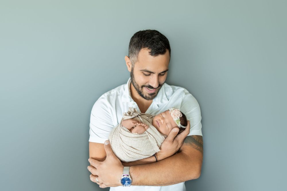 A person in a white t-shirt holds and comforts a small grey kitten against their chest.