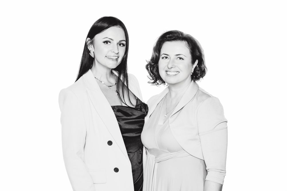 Black and white photo of two individuals in business attire standing close together in a studio setting.