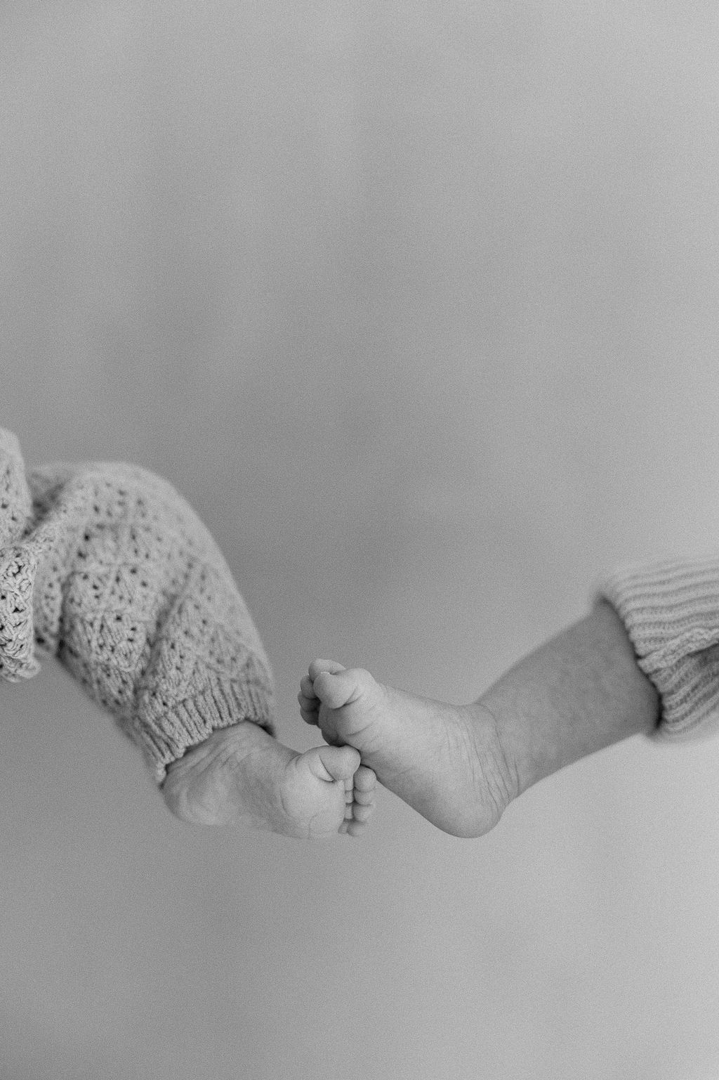Black and white artistic photograph of baby feet wearing knitted booties against a light background.