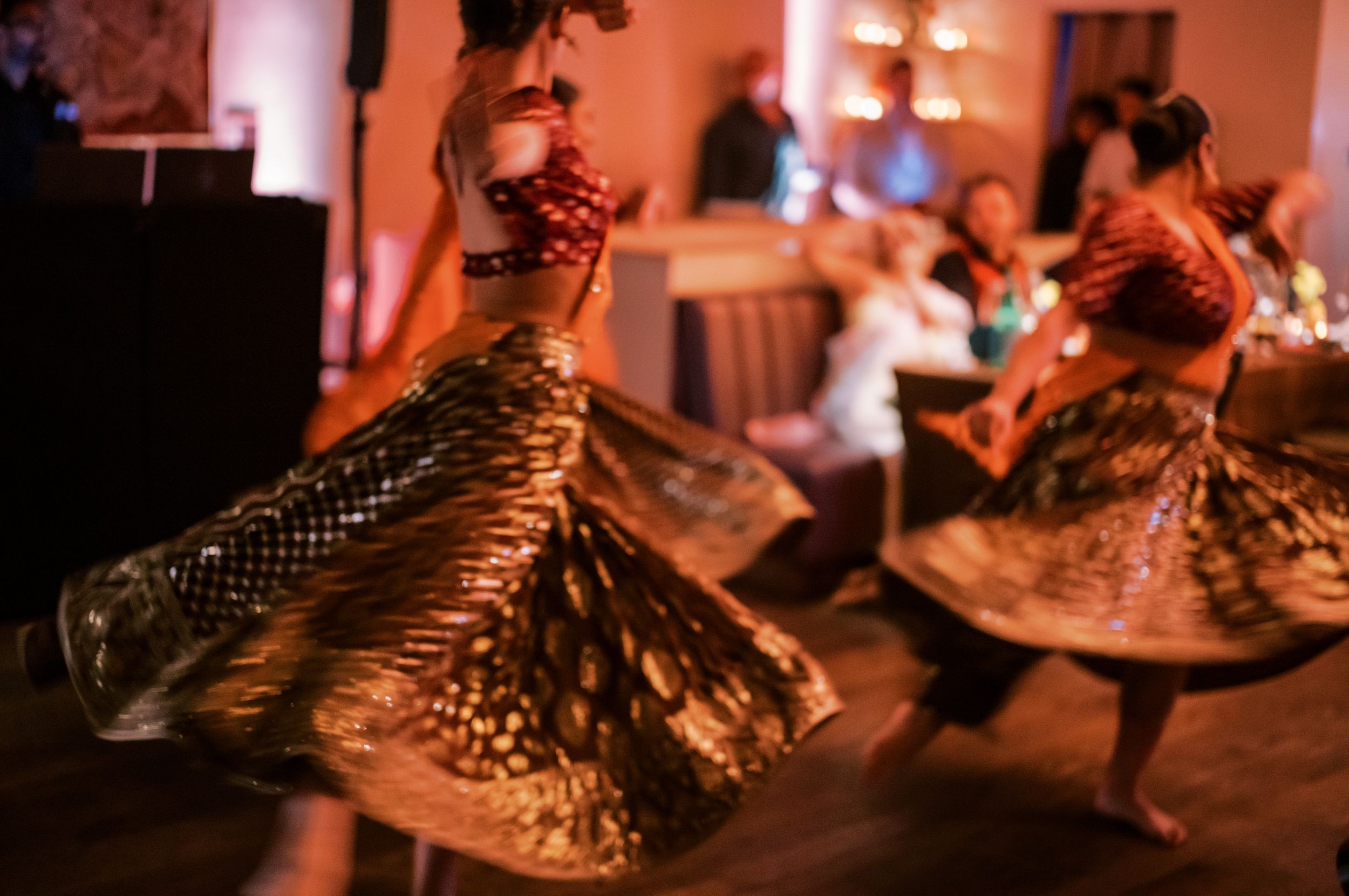 Dancers in flowing gold dresses spinning and twirling on a dimly lit dance floor.