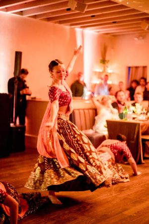 A dancer in a red and gold dress performs a dramatic spin on a wooden dance floor at an event.