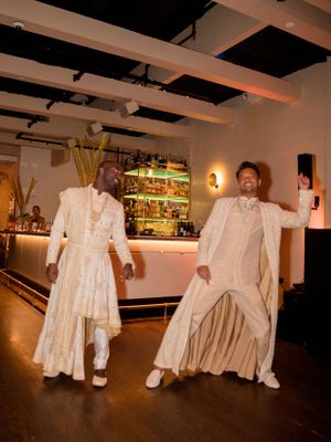 Two people in flowing white outfits dancing together in front of an illuminated bar.